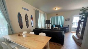 Un coin repas avec une table en bois et des chaises blanches, un canapé noir en arrière-plan et une enseigne sur le mur indiquant « ATLANTIC CITY, NJ ».