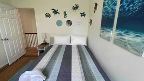 Une chambre à coucher comprenant un lit, une table de chevet, un mur décoré sur le thème de la mer et une grande fresque représentant l’océan.