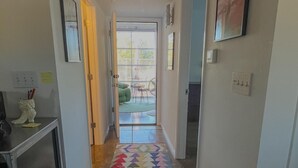 Un couloir agrémenté d’un tapis coloré, une porte donnant sur un balcon et une petite table ornée d’objets décoratifs.
