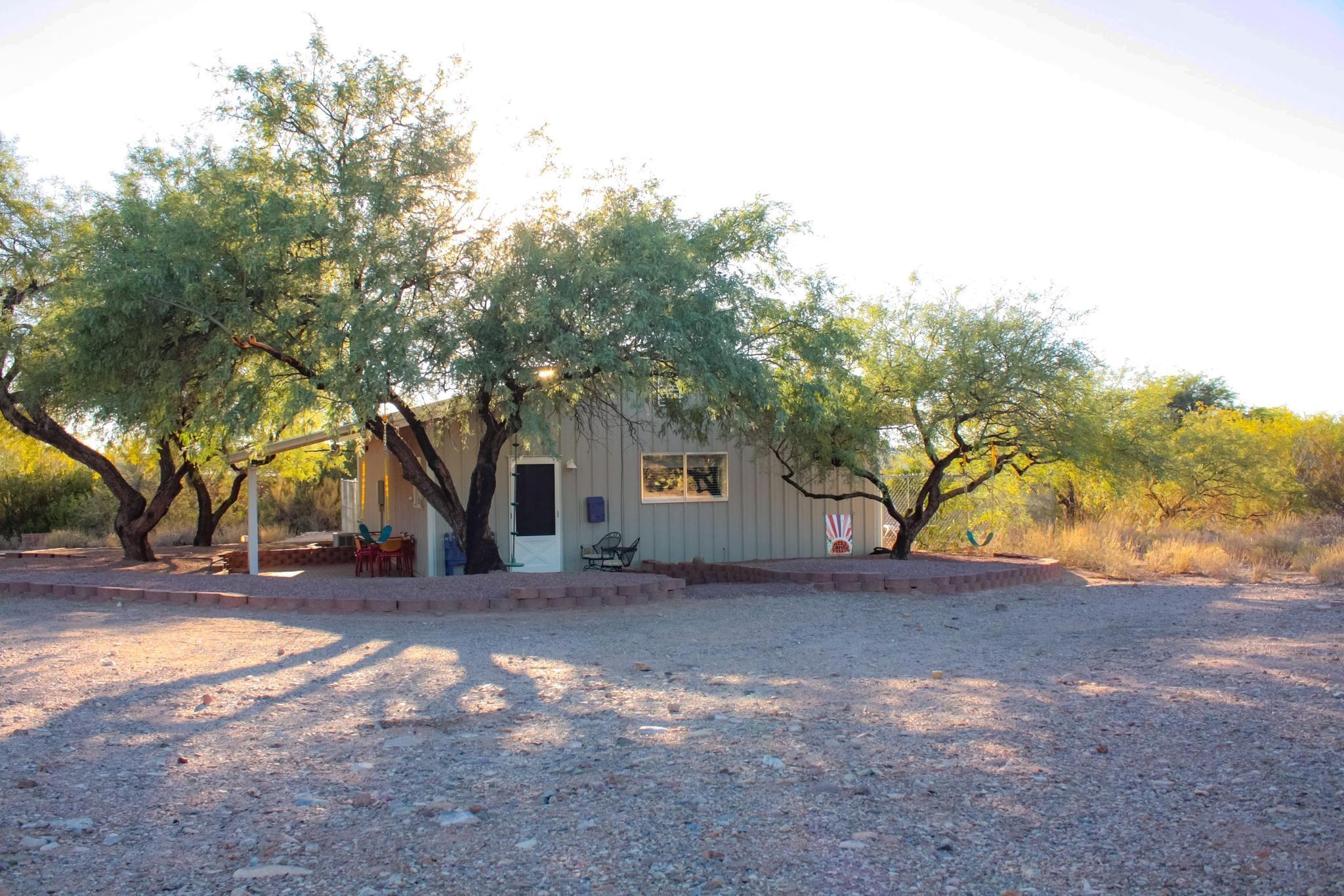 A small, single-story building with a door and windows, surrounded by gravel and trees.
