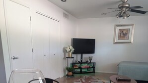 Un coin repas avec une nappe à motifs floraux, un vase en verre contenant des fleurs et un téléviseur posé sur un meuble.