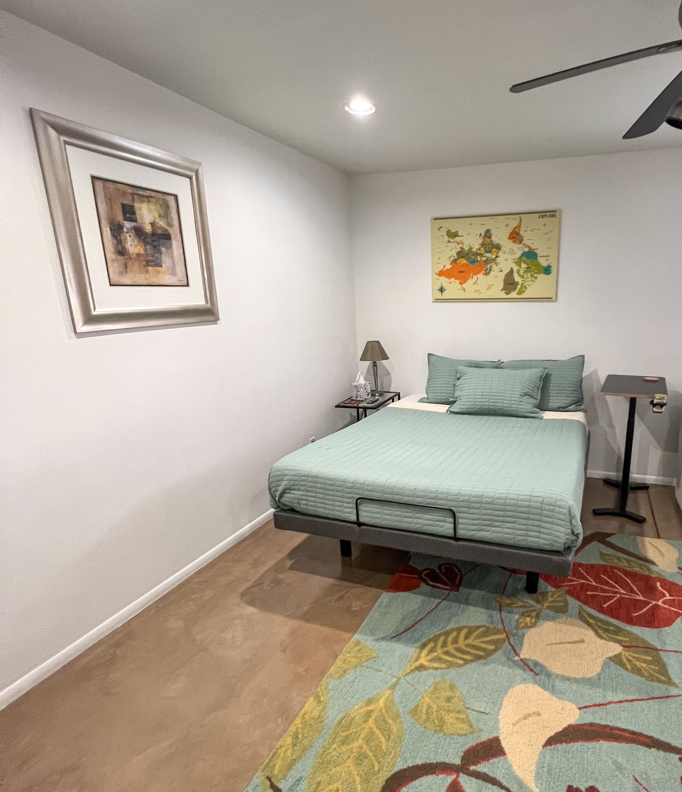A bedroom with a bed, a nightstand, a lamp, a framed picture, and a map on the wall.