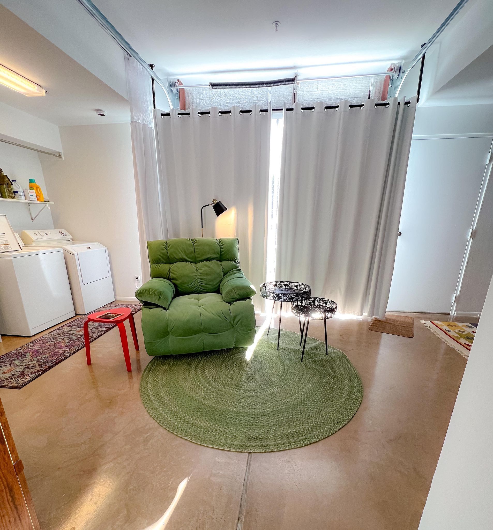 Ein Wohnzimmer mit einem grünen Sofa, einem kleinen runden Tisch, einer Stehlampe und einer Waschmaschine.