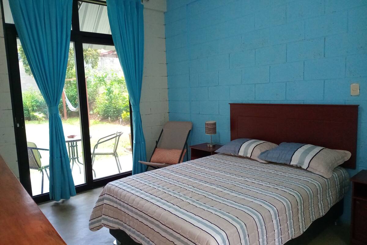 A bedroom with a bed, a chair, a nightstand, and a view through a glass door.