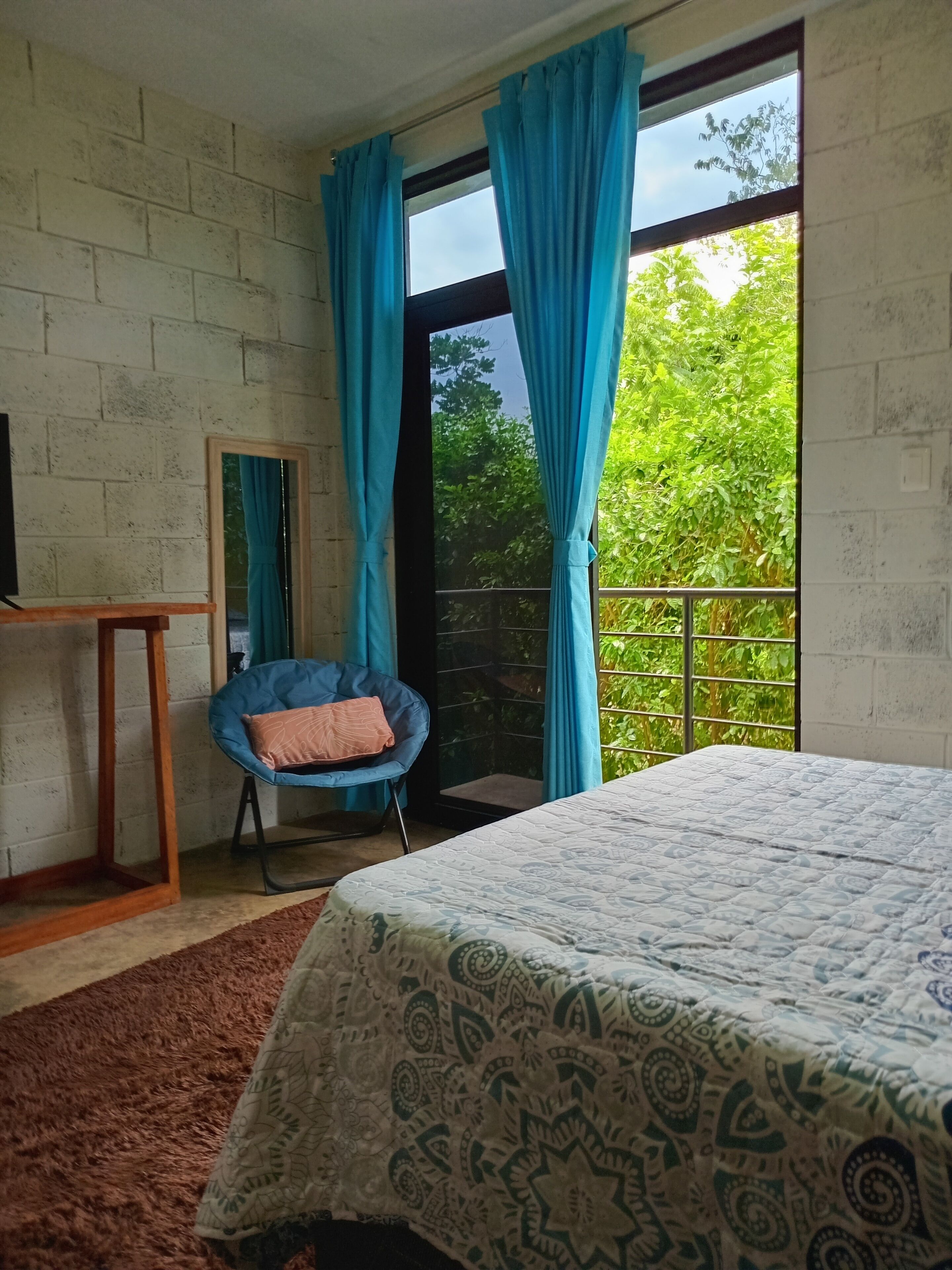 A bedroom with a bed, a chair, a TV, and a balcony with curtains.