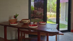 A wooden table with bowls and a basket, a bench, and a view through a glass door to an outdoor area with greenery.
