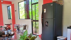 A modern kitchen with a black refrigerator, a dining table with chairs, and a large window with a view of greenery.