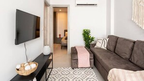 Ein modernes Wohnzimmer mit Flachbildfernseher, einer Couch, einem gemusterten Teppich und einer Zierpflanze.
