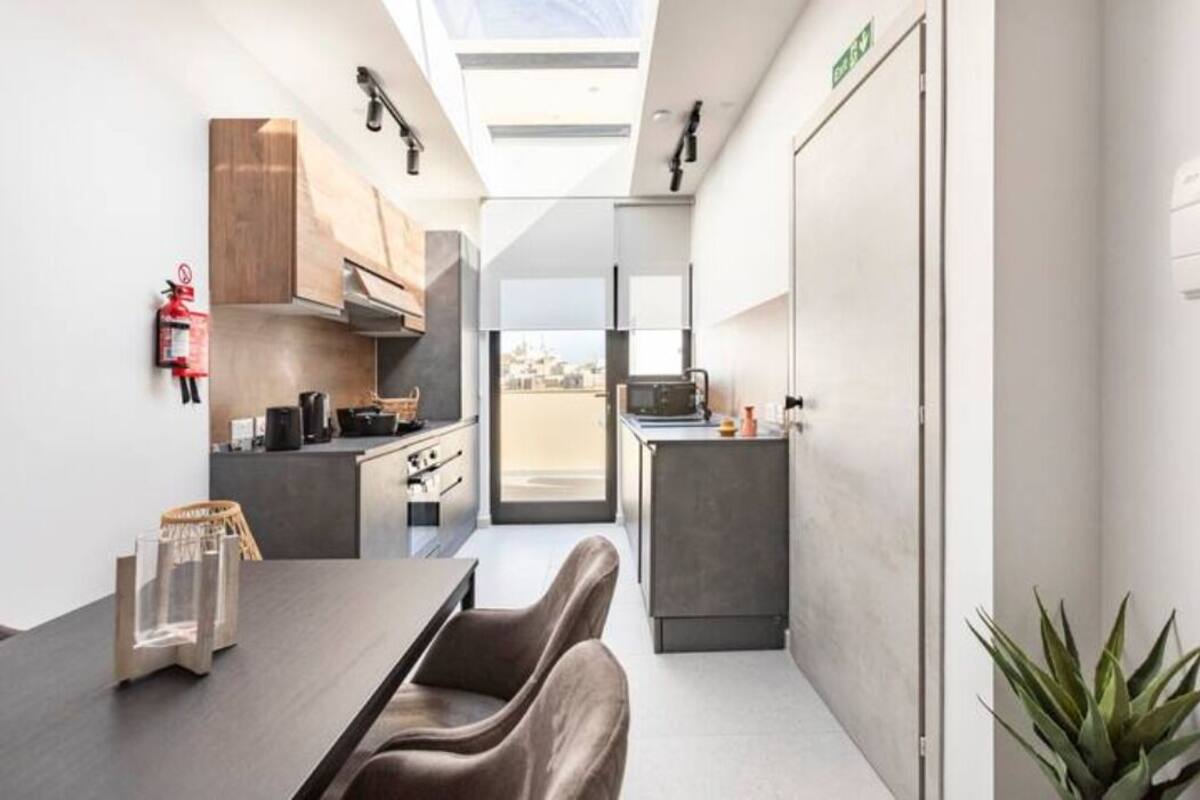 A compact kitchen with modern appliances, a dining area with a table and chairs, and a view through a glass door.