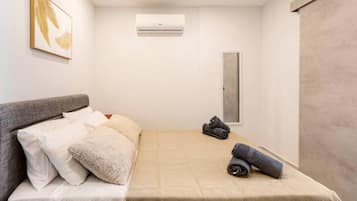 A modern bedroom with a bed, pillows, a wall-mounted air conditioner, and a framed artwork.