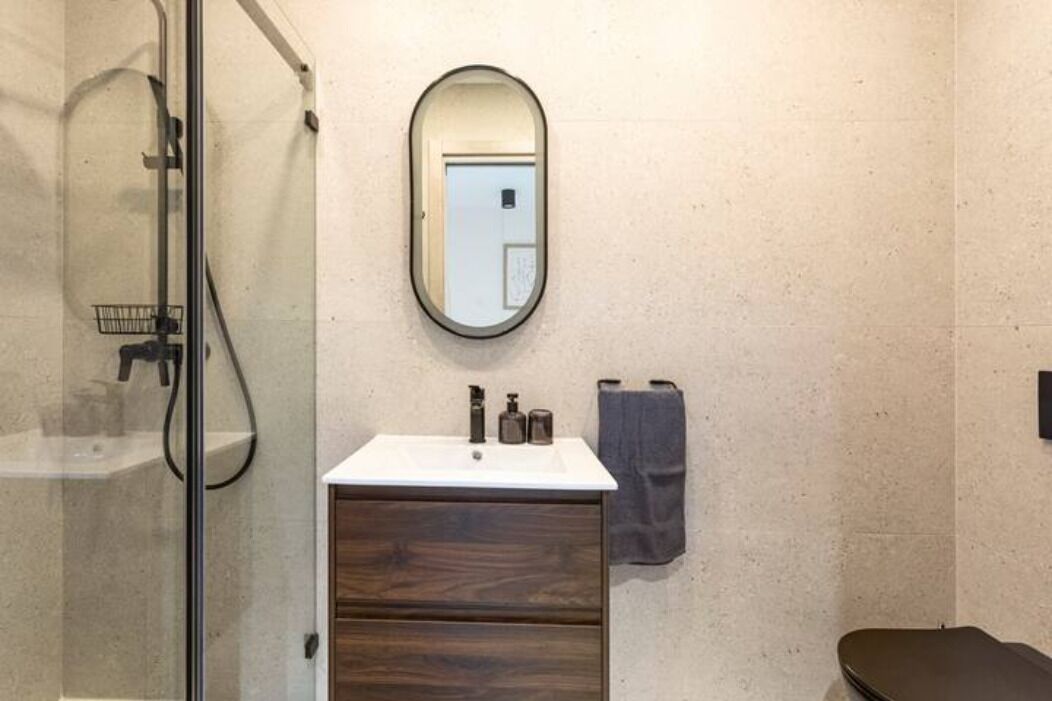 A bathroom with a glass shower enclosure, a wooden vanity with a white sink, a mirror, and a towel rack.
