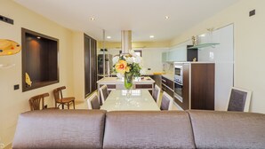 Un salon moderne avec un grand canapé, une table à manger avec des chaises et, au fond, un coin cuisine.