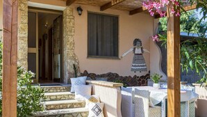 A covered outdoor seating area with stone steps, a mural, and a table with chairs. - Elegant deluxe cottage close to beaches (Sardegna)