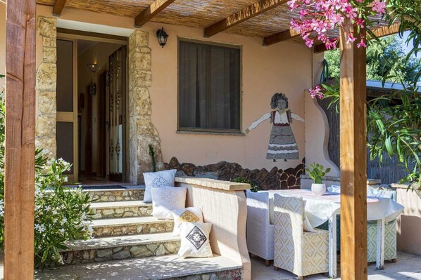 A covered outdoor seating area with stone steps, a mural, and a table with chairs.