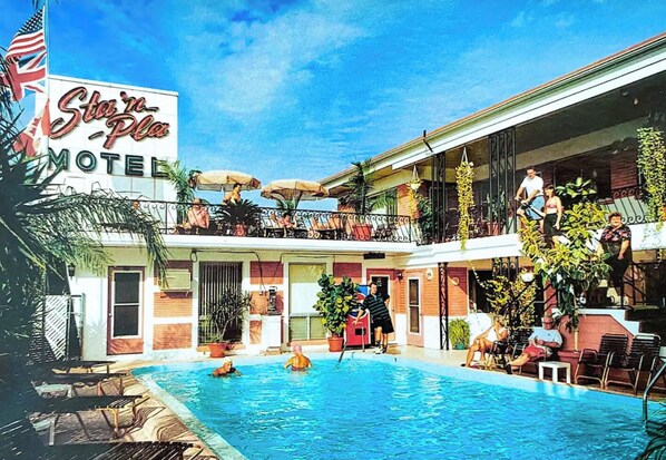 A motel with a swimming pool, outdoor seating, and a balcony with umbrellas.