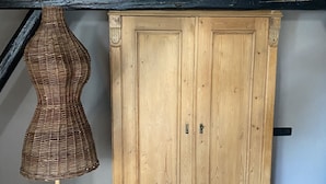 Ein Holzschrank mit zwei Türen und Griff, eine Korbtreppe auf einem Holzfuß und ein schwarzer Metallbalken darüber.