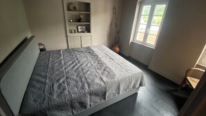Ein Schlafzimmer mit einem Bett, einem Fenster, einem Regal mit Dekoration und einer Pflanze.