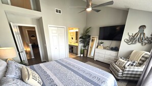 A bedroom with a bed, a chair, a dresser, a television, and a ceiling fan.