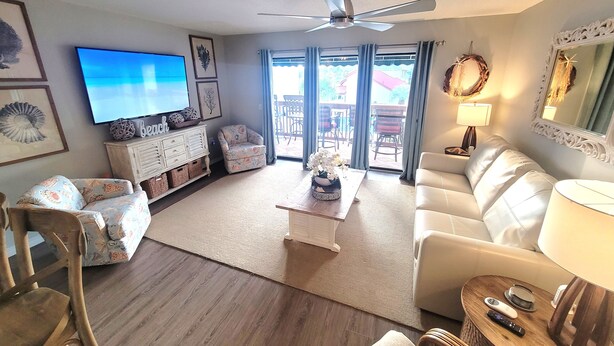 A living room with a flat-screen TV, a ceiling fan, a sofa, a coffee table, and a dining area with chairs and a table.