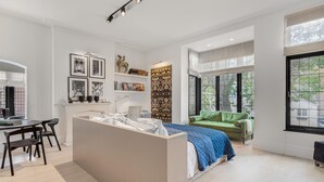 Et moderne soveværelse med en stor seng, en grøn sofa, et skrivebord med stole og en bogreol.