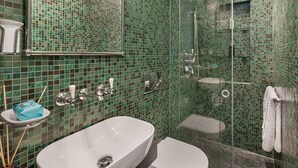 Et badeværelse med væg af grønne mosaikfliser, en hvid vask, en brusekabine med glasvægge og et toilet.
