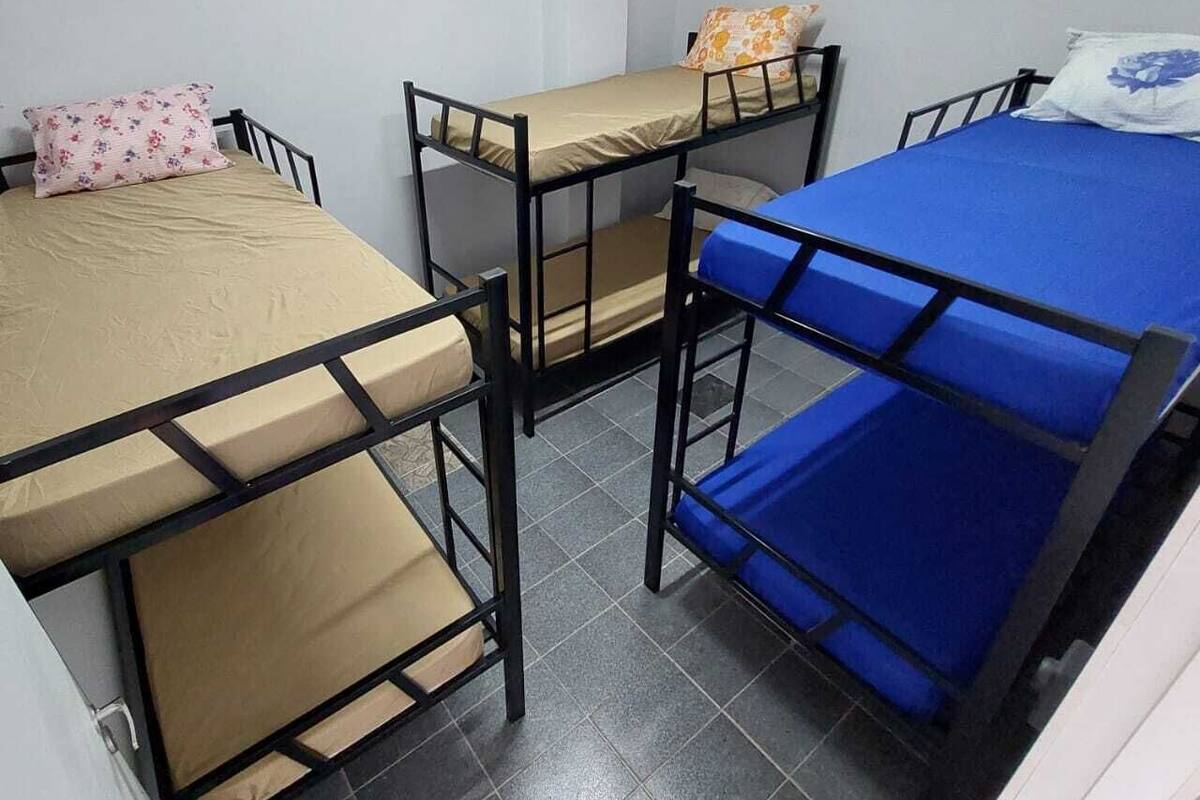 A dormitory room with bunk beds, a white wall, and a tiled floor.