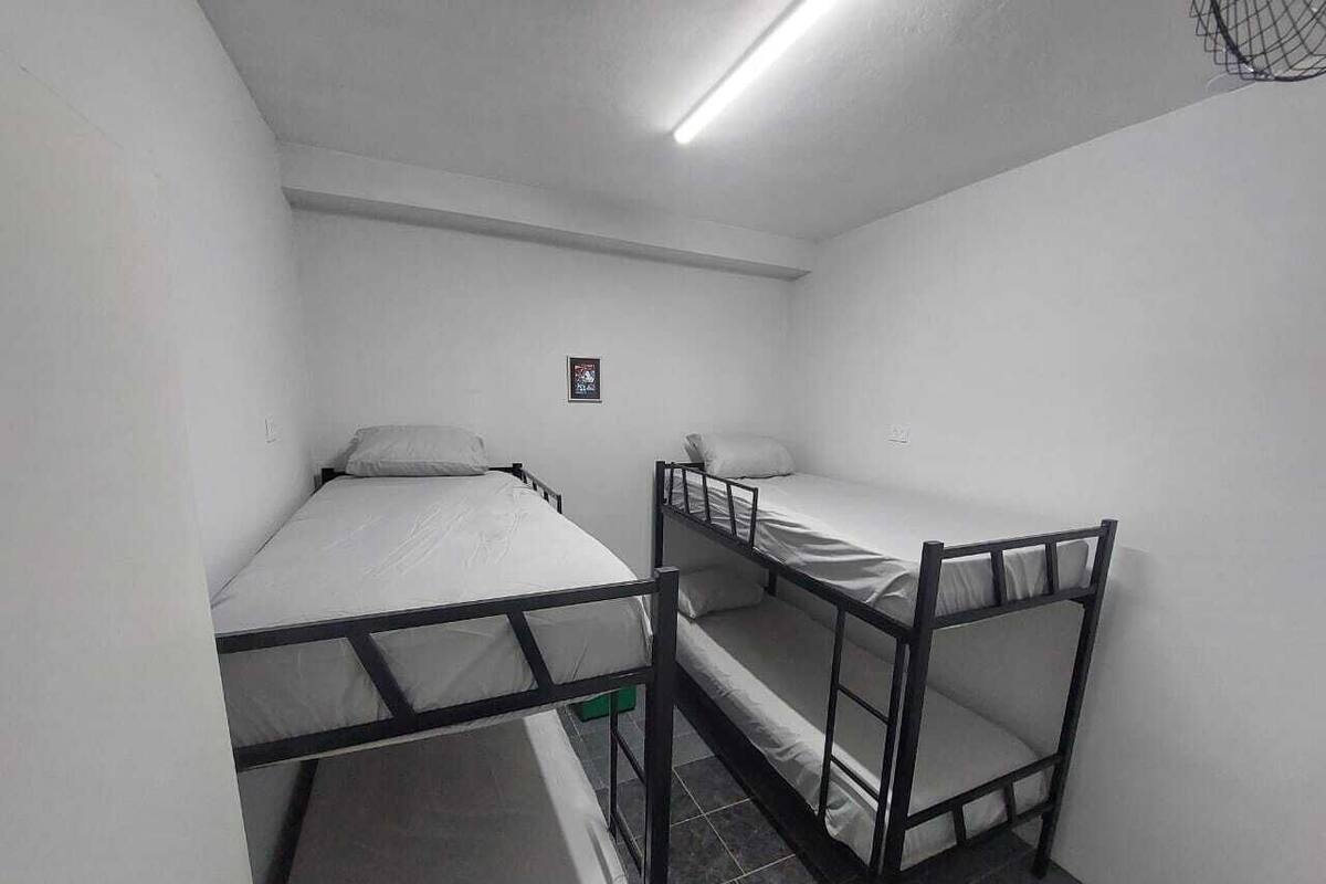 A dormitory room with bunk beds, a small framed picture on the wall, and a ceiling light.