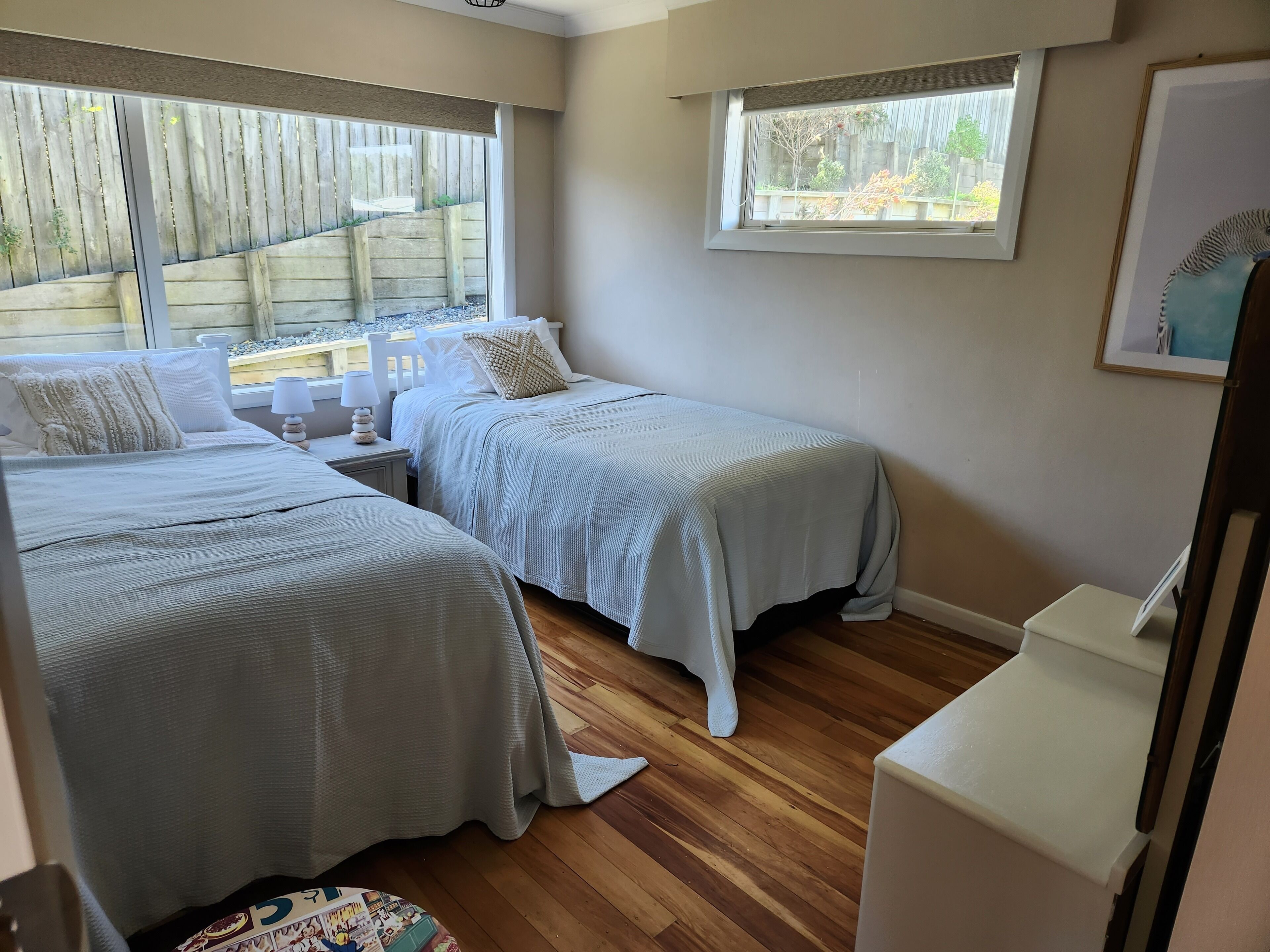 A bedroom with two beds, a window, and a small table with a lamp.