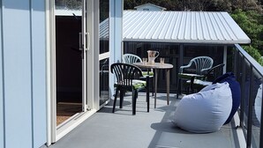 A balcony with a table and chairs, a bean bag, and a sliding glass door leading to an interior space. - # 40 At the Beach (Waitārere Beach)
