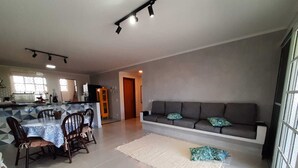 Una sala moderna con un sofá, una mesa de comedor con sillas y una cocina al fondo.