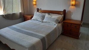 Un dormitorio con una cama de madera, dos mesitas de noche, una ventana con cortinas e iluminación en la pared.