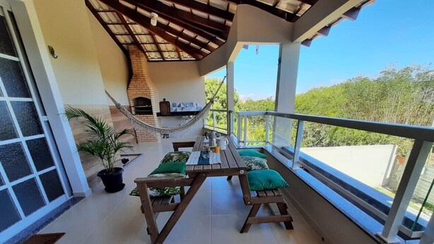 Un espacio al aire libre techado con una hamaca, una mesa con bancos y vista a la vegetación.