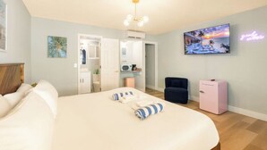 A hotel room with a large bed, a TV mounted on the wall, a pink minibar, and a neon sign.
