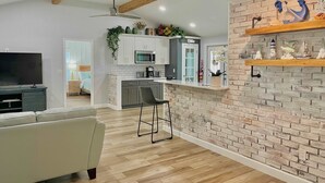 A modern kitchen with white cabinets, a microwave, and a coffee maker. There is a wooden ceiling with exposed beams and a ceiling fan.