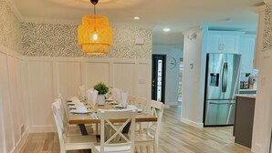 A dining area with a wooden floor, white chairs, a table set for four, and a hanging light fixture.
