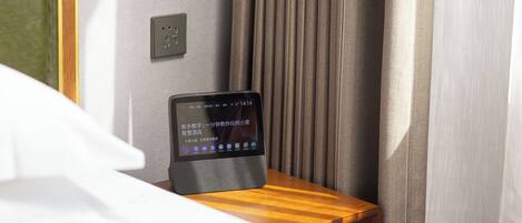 A tablet on a wooden nightstand in a hotel room, with a curtain and a wall socket visible.