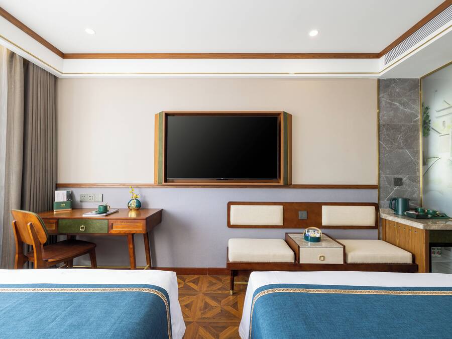 Ett hotellrum med två sängar, ett skrivbord, en stol, en tv och ett badrum med spegel och handfat.