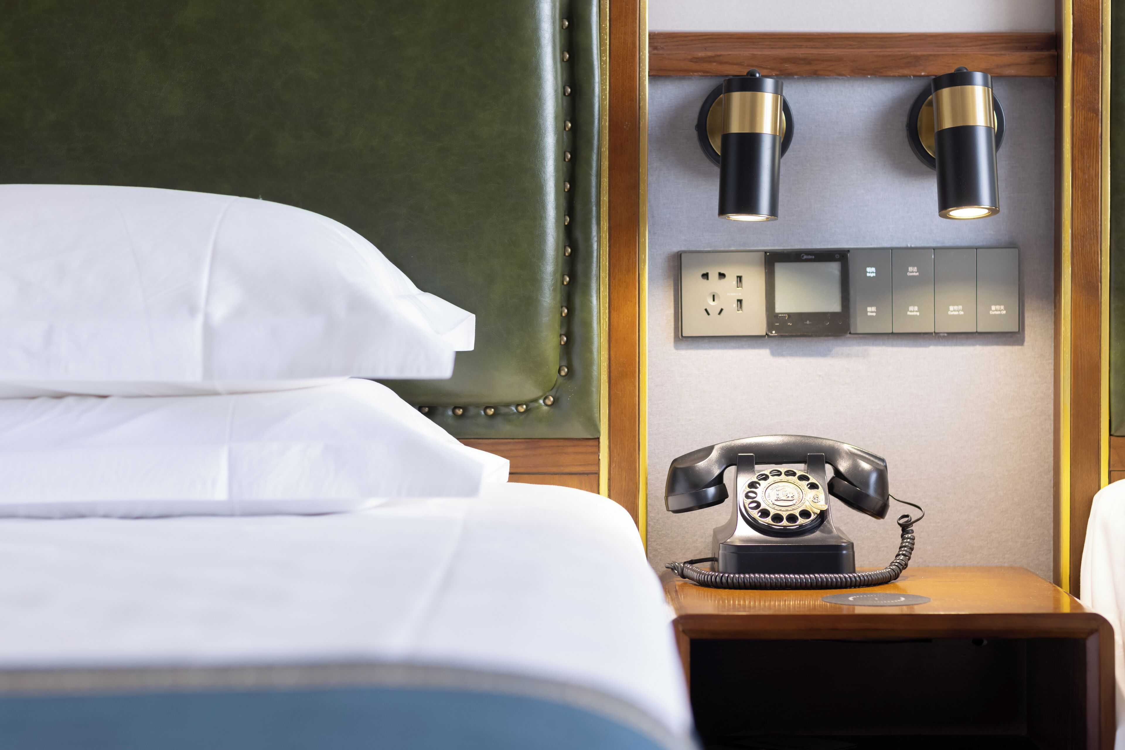 A hotel room with a bed, a bedside telephone, and two wall-mounted lamps.