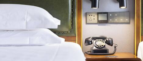 A hotel room with a bed, a bedside telephone, and two wall-mounted lamps.