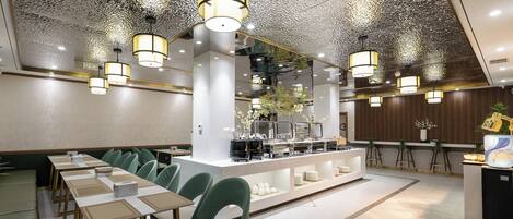 Un comedor moderno con una estación de buffet central, sillas tapizadas en verde e iluminación colgante.