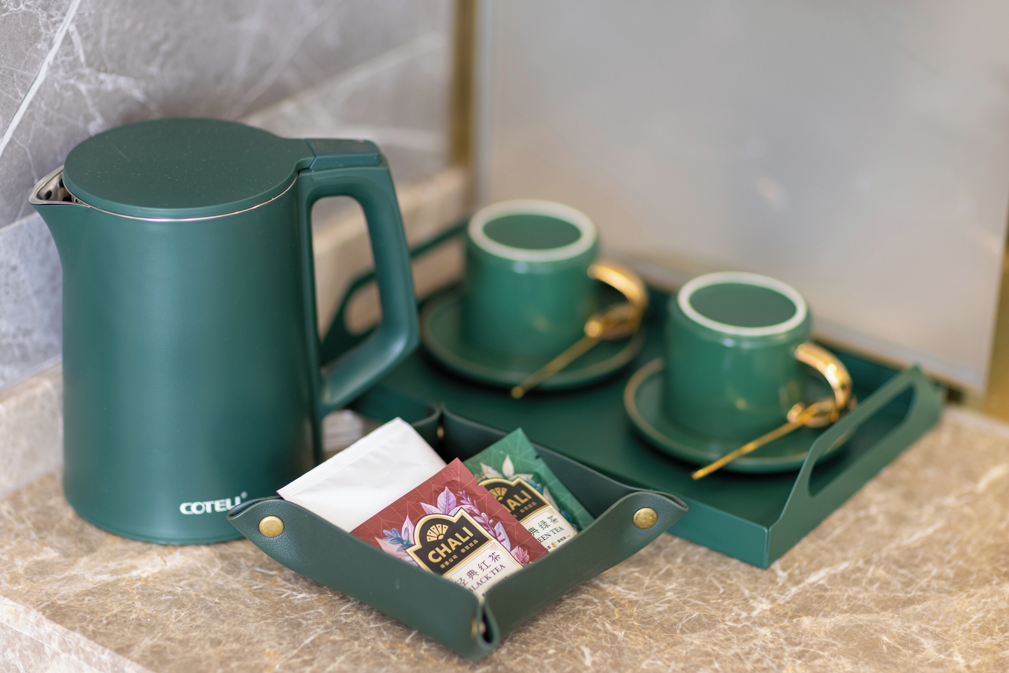 A tea set with a green kettle, cups, and saucers on a marble countertop.