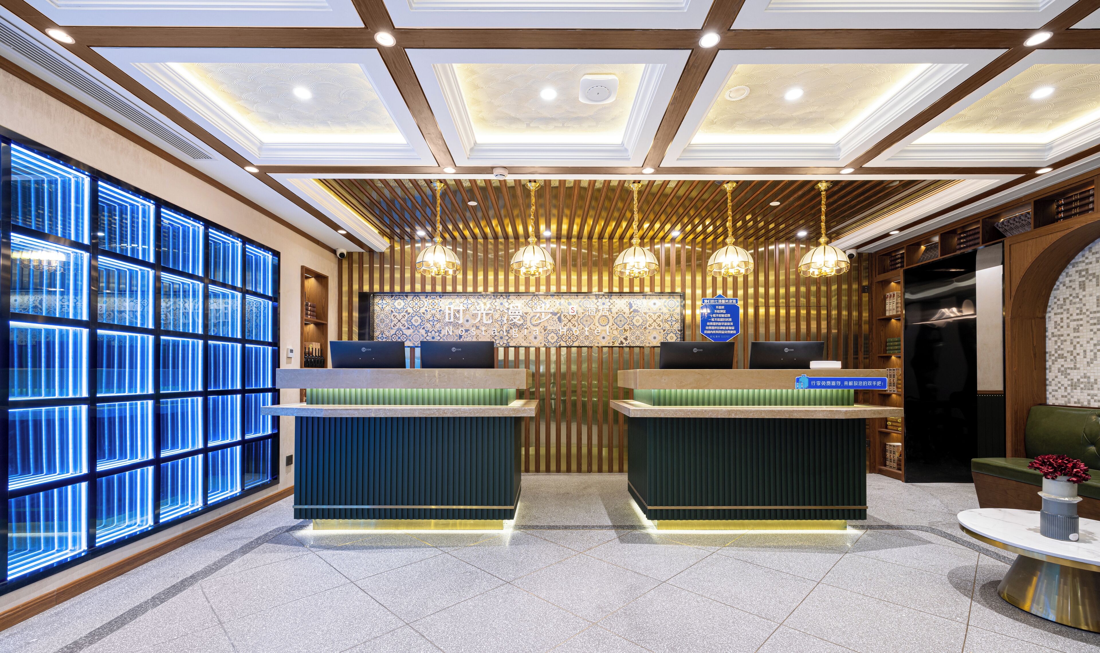 A hotel reception area with two reception desks, a patterned wall, and a ceiling with recessed lighting.