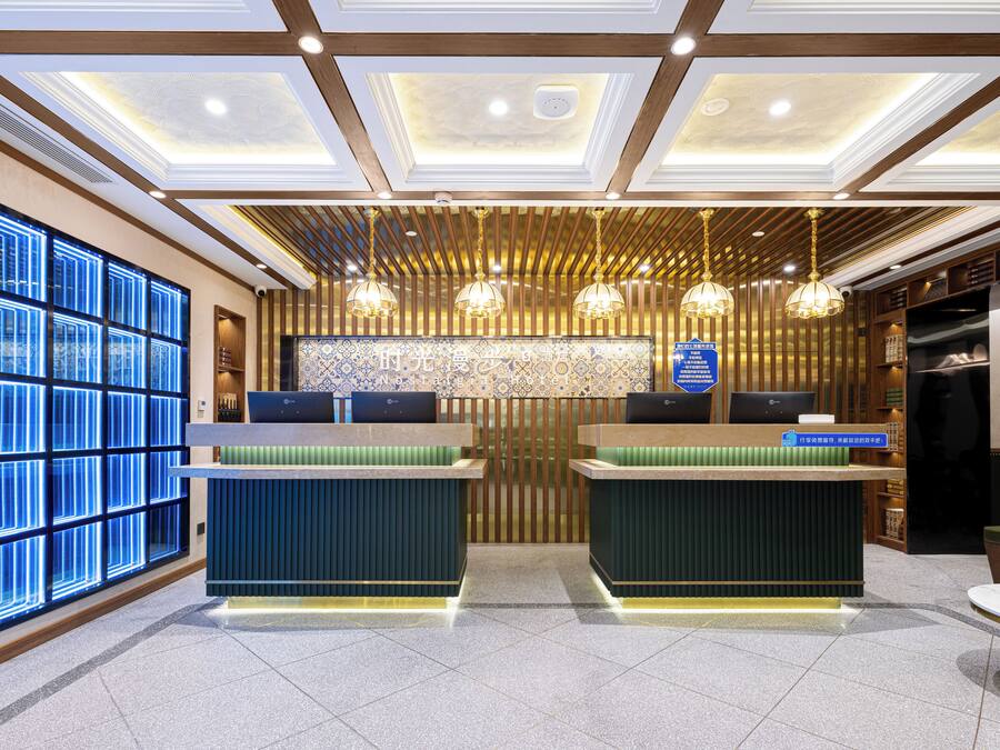 Zona de recepción de un hotel con dos mostradores, un muro con diseño y un techo con iluminación empotrada.