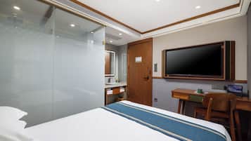 Ein Hotelzimmer mit Bett, Schreibtisch, Stuhl, Fernseher und einem Badezimmer mit Spiegel und Waschbecken.