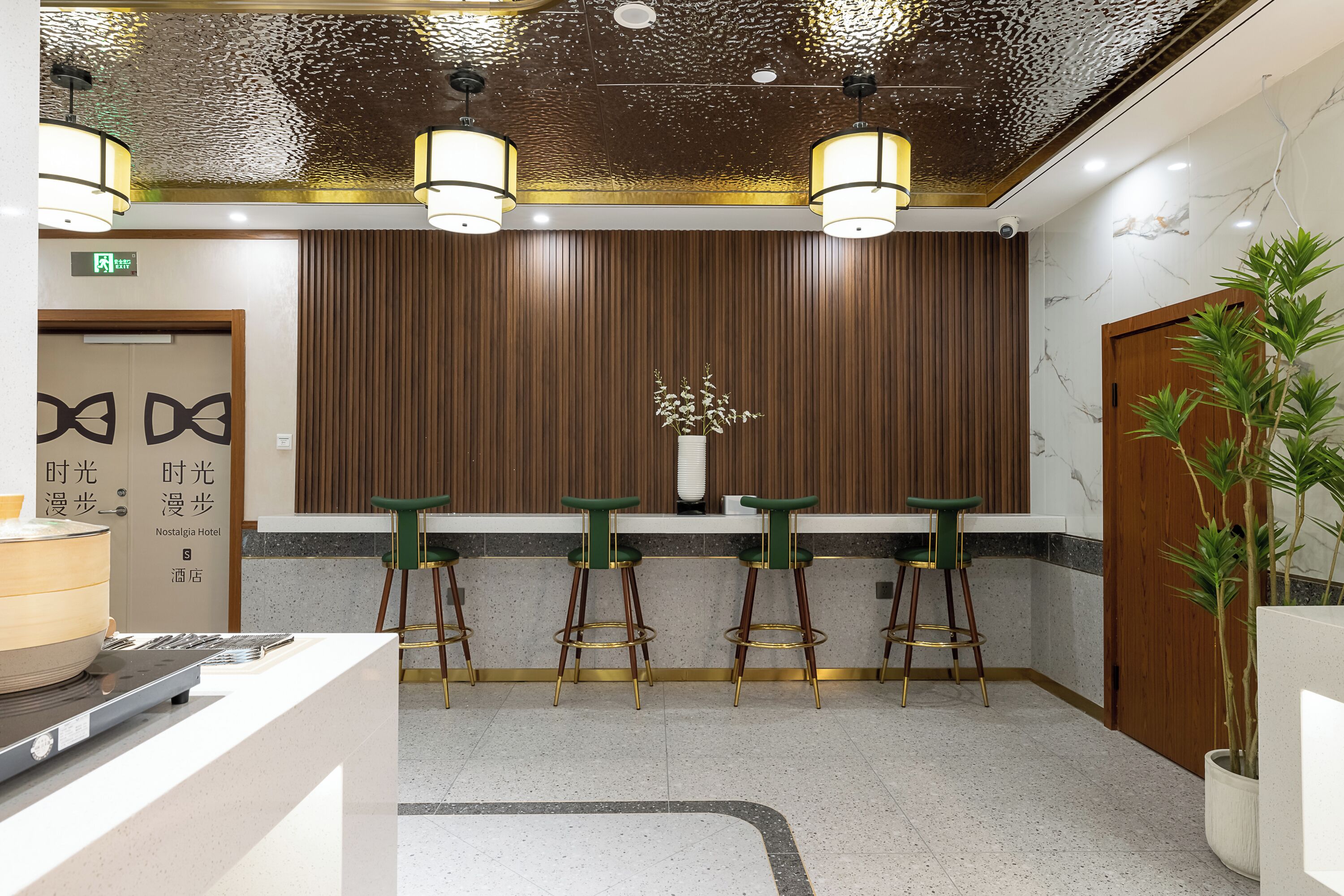 Un'area reception con parete rivestita in legno, una scrivania e tre sgabelli verde bar.