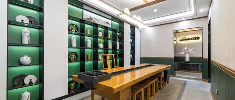 A modern interior with a long wooden table and benches, green shelving with decorative items, and a sign indicating a restaurant or dining area.