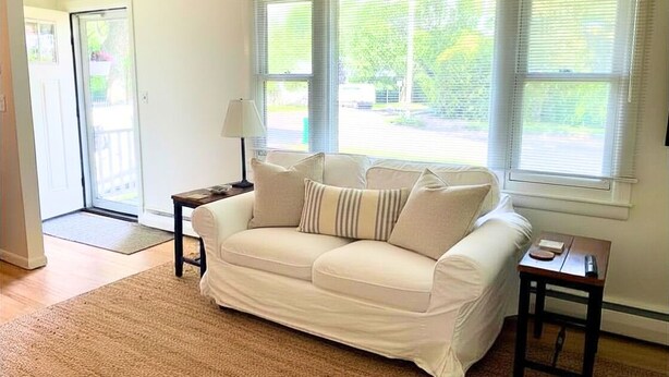 Ein Wohnzimmer mit einer Couch, einer Lampe, einem kleinen Tisch und einem Fenster mit Jalousien.