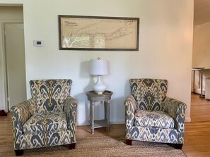 Une pièce comprenant deux fauteuils à motifs, une petite table avec une lampe et une carte encadrée accrochée au mur.