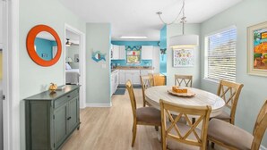 Een eetruimte met een ronde tafel en stoelen, een keuken op de achtergrond en een gang naar een andere kamer.