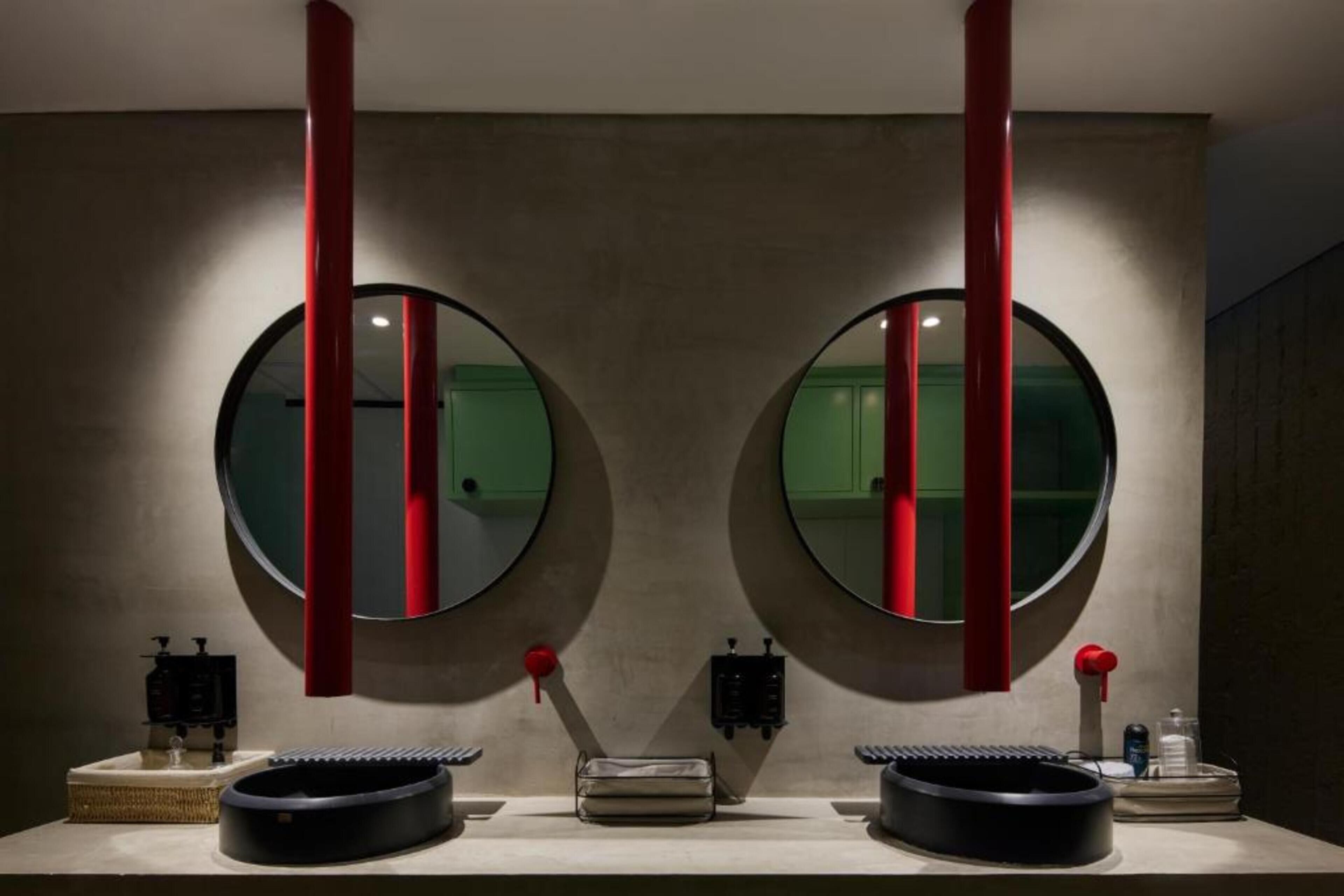 A bathroom with two round mirrors, red vertical accents, and a central sink with toiletries.